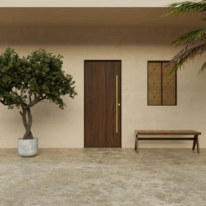 Modern walnut exterior door with brass pull handle, showcased in a minimalist outdoor entry with tree and bench.