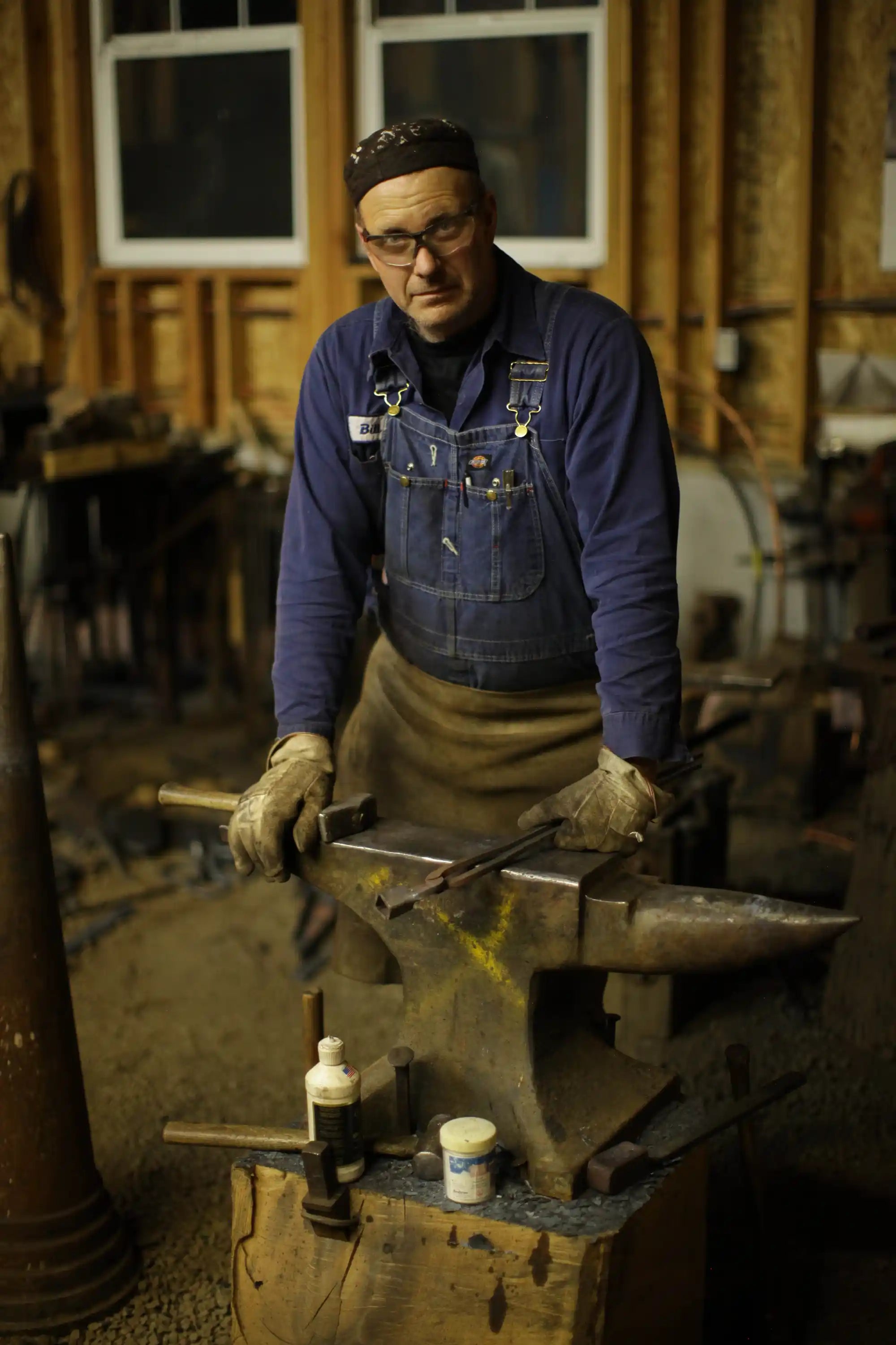Blacksmith holding forging tools on top of an anvil and looking at the camera.