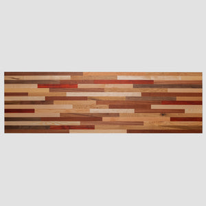 A long, horizontal wood countertop wall art piece made of various solid colors and patterns in reds, browns, yellows, and other earth tones. The background is white with no shadows or textures on it. This artwork would be used as an accent for the dining room table, sitting under that wall art, and to match its color scheme.