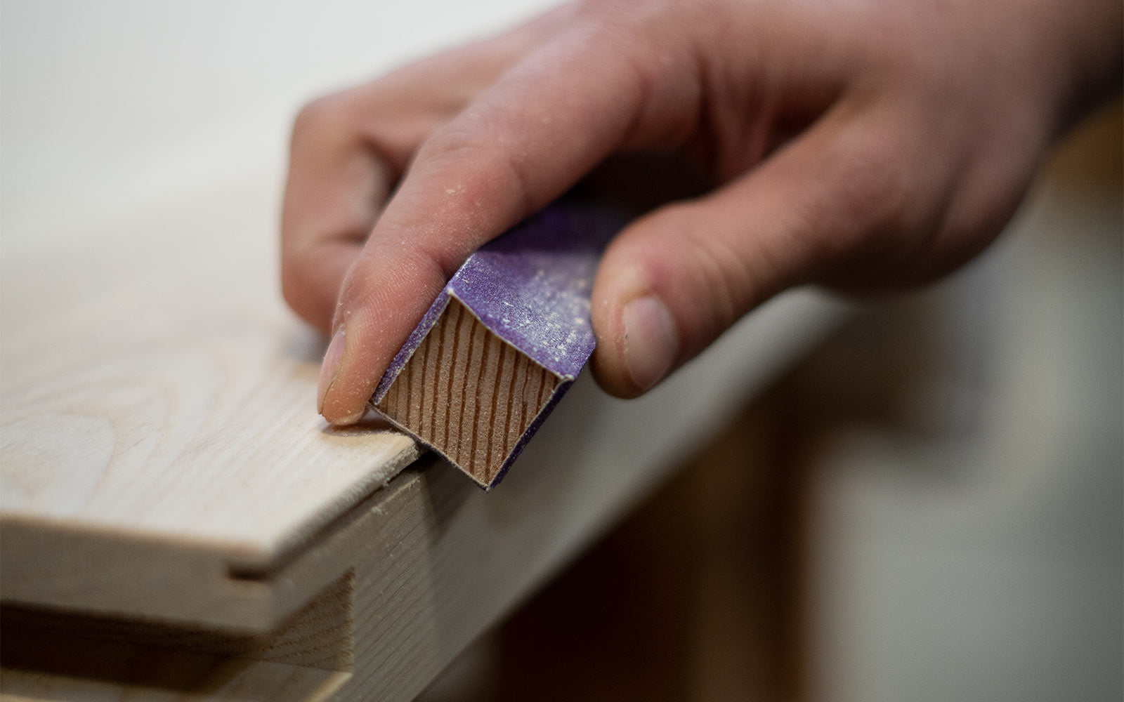 Craftsman hand using a small sanding cube to finish a door's bottom.