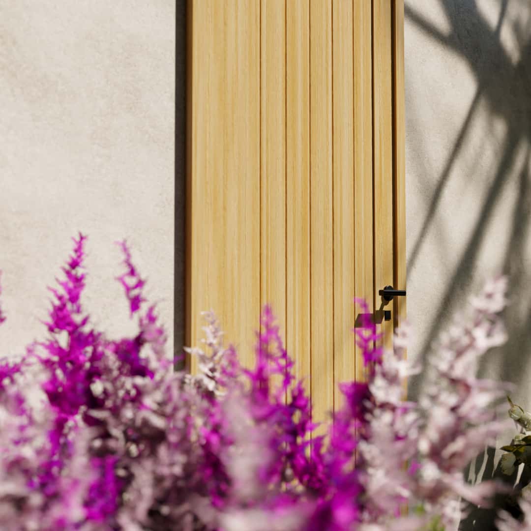 Maple Wood Modern Flush Plank Solid Core Exterior Front Door next to white and pink flower bushes