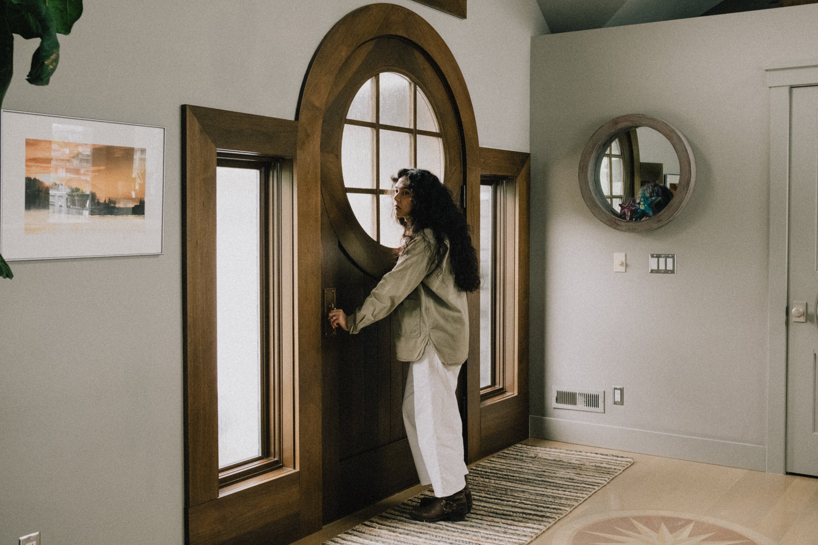 Woman stands at a round top door in the entryway of a house holding the doorknob