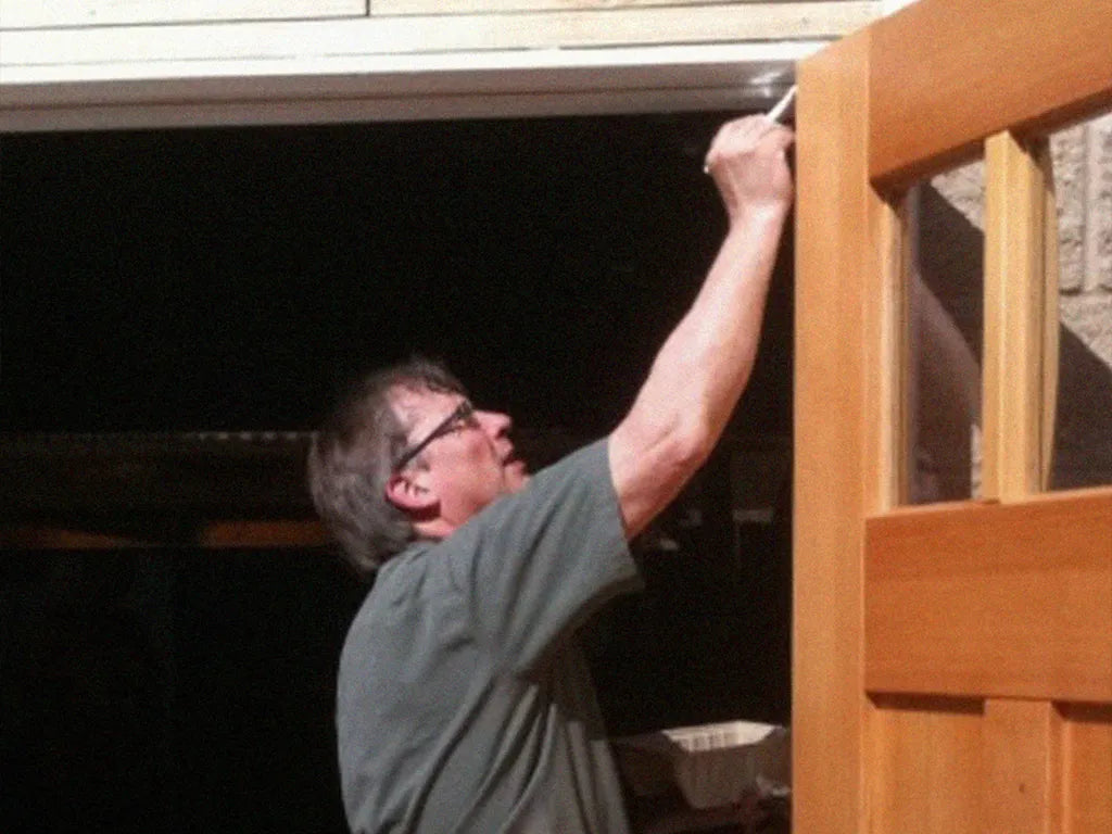 A woodworking man who is adding finish to a wooden garage carriage door