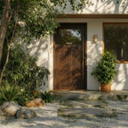 Laguna Chevron Paneled Solid Wood Exterior Door With Window and chevron panels on a white wall, surrounded by greenery