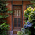 Custom Mixed wood species entry door on a red wall in a garden setting.