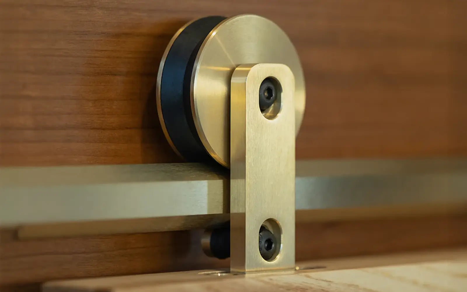 Close-up of a modern sliding door hardware with a brushed brass wheel and arm on a wooden door. The design is sleek and contemporary.