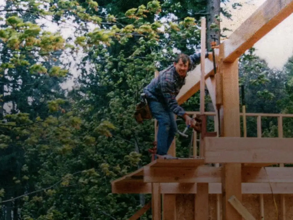 A woodworker looking at the camera while working on a wooden housing structure