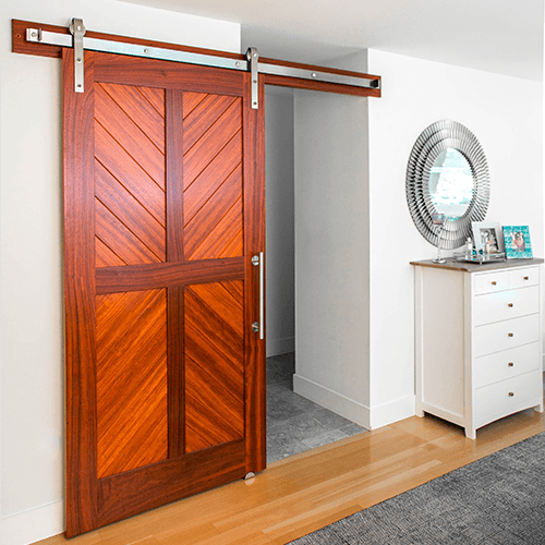 Padauk wood chevron barn door with stainless steel hardware in a bedroom space