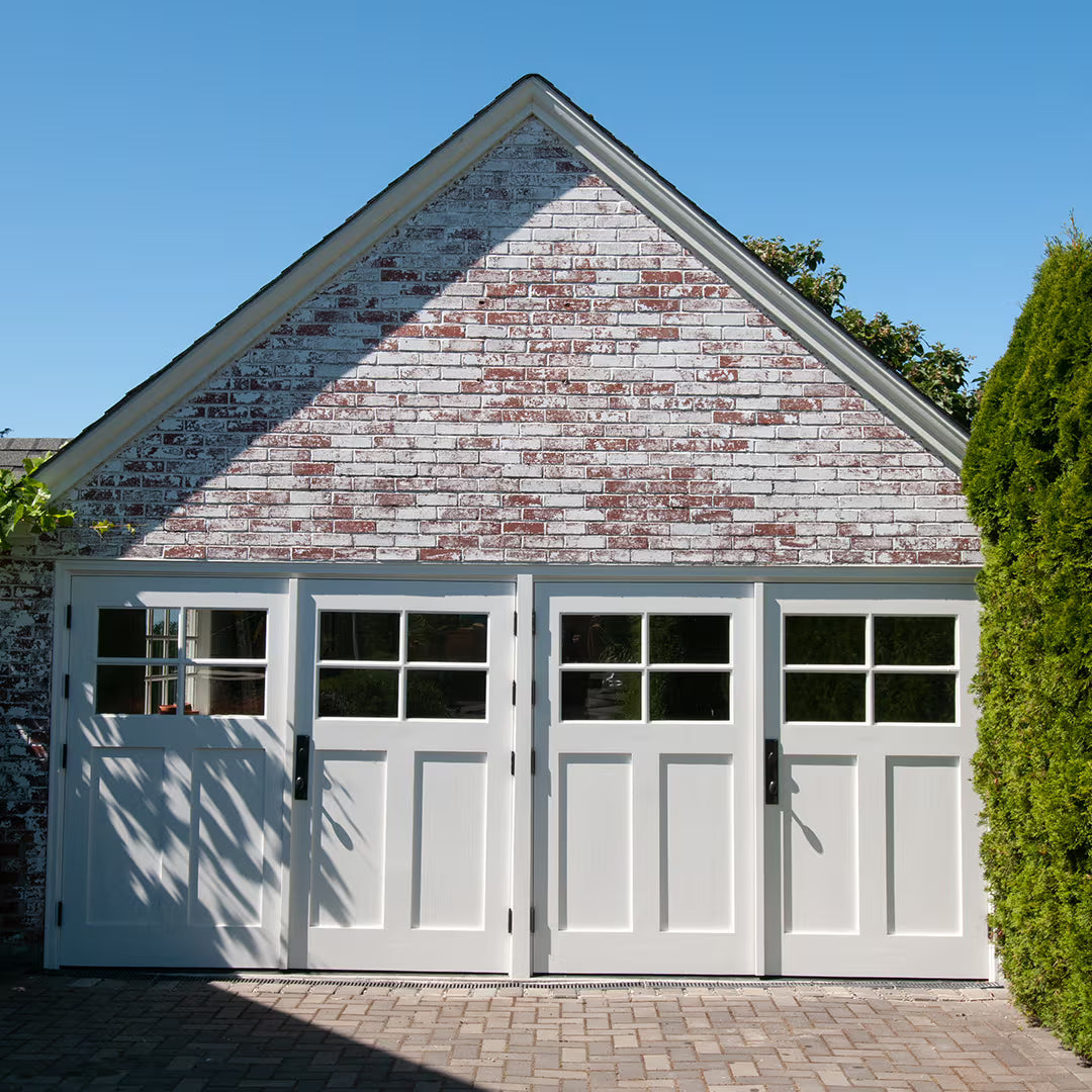 White carriage doors with four-panel window design on each door on a clear blue sky. 