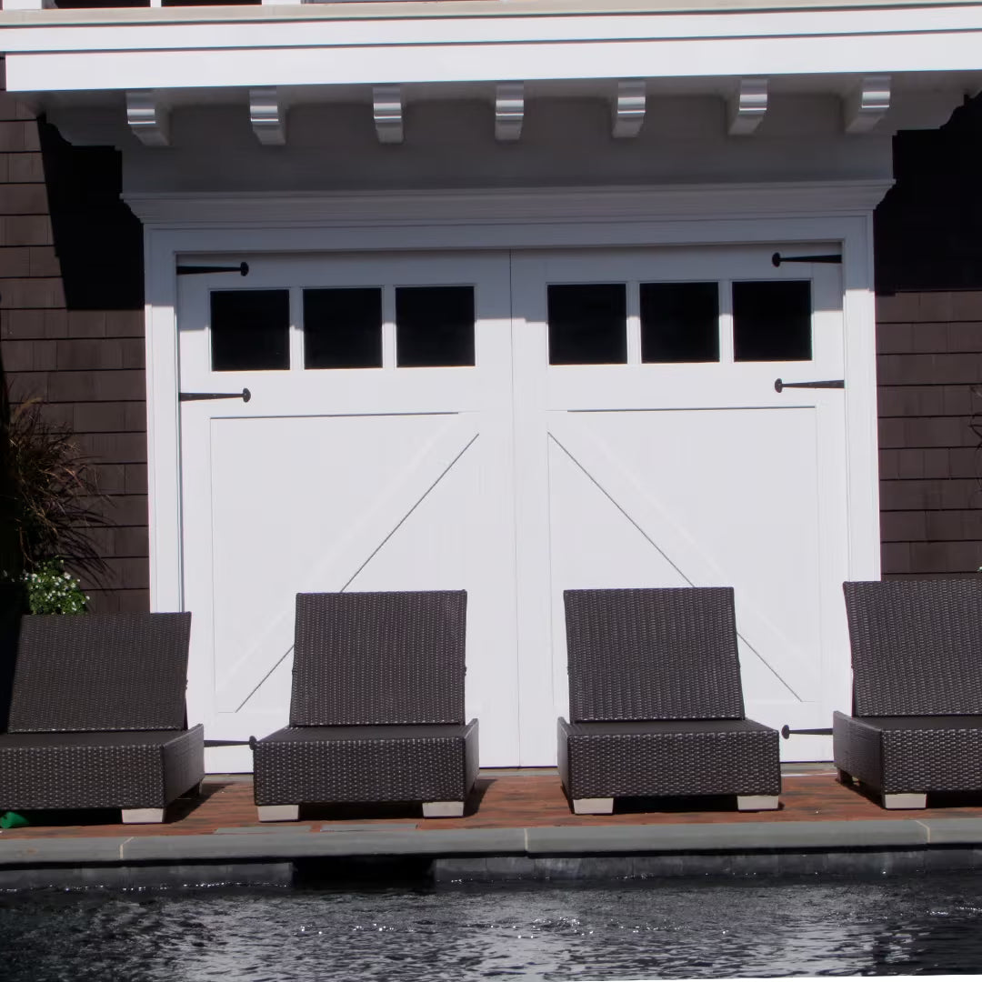 White Z-brace carriage garage door with short strap hinges, shown on a bright residential exterior near a pool or spa area in daylight.