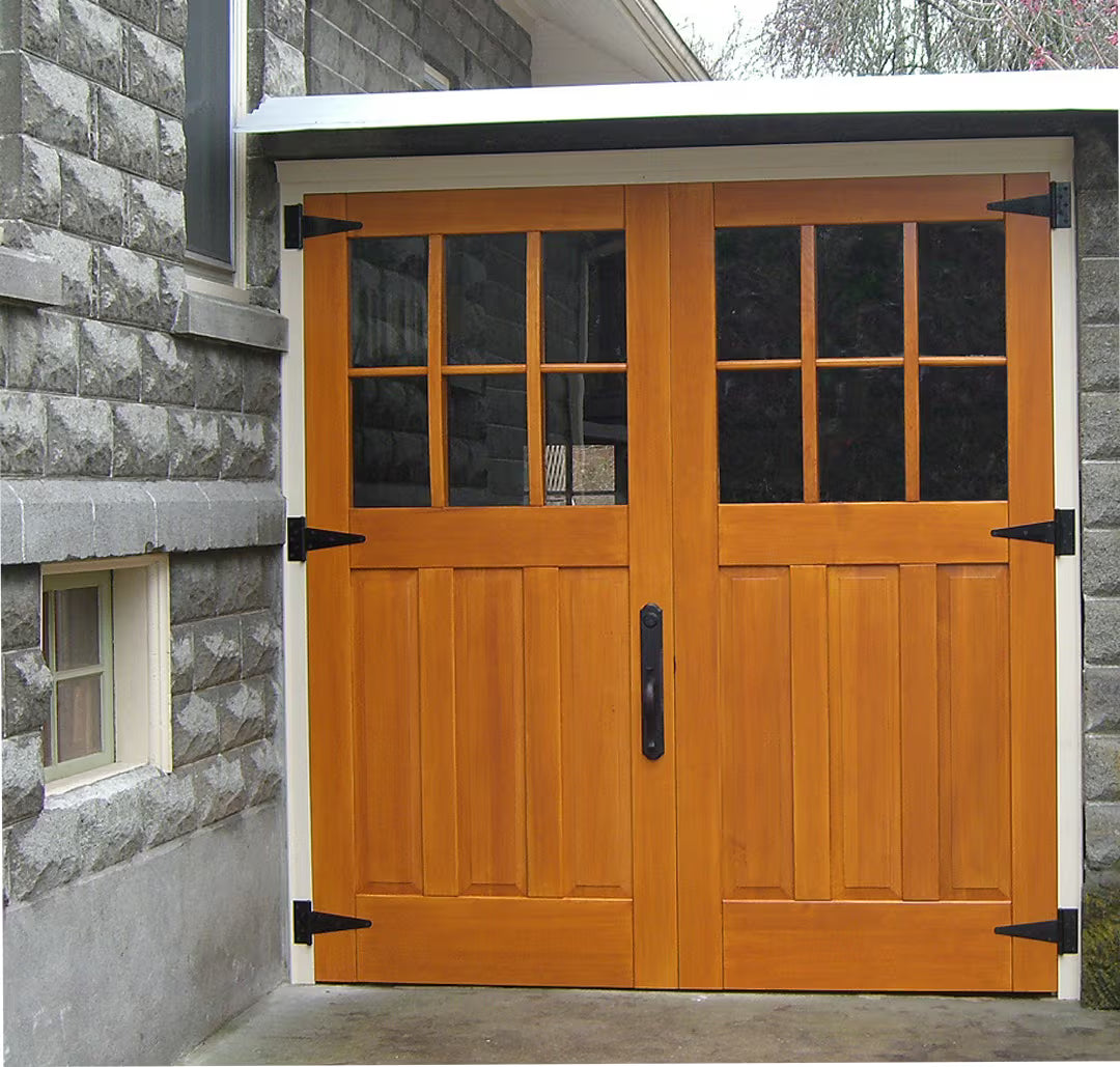 Carriage-style garage door with clear glass panels and triangular metal hinges, shown on a residential exterior in natural daylight.