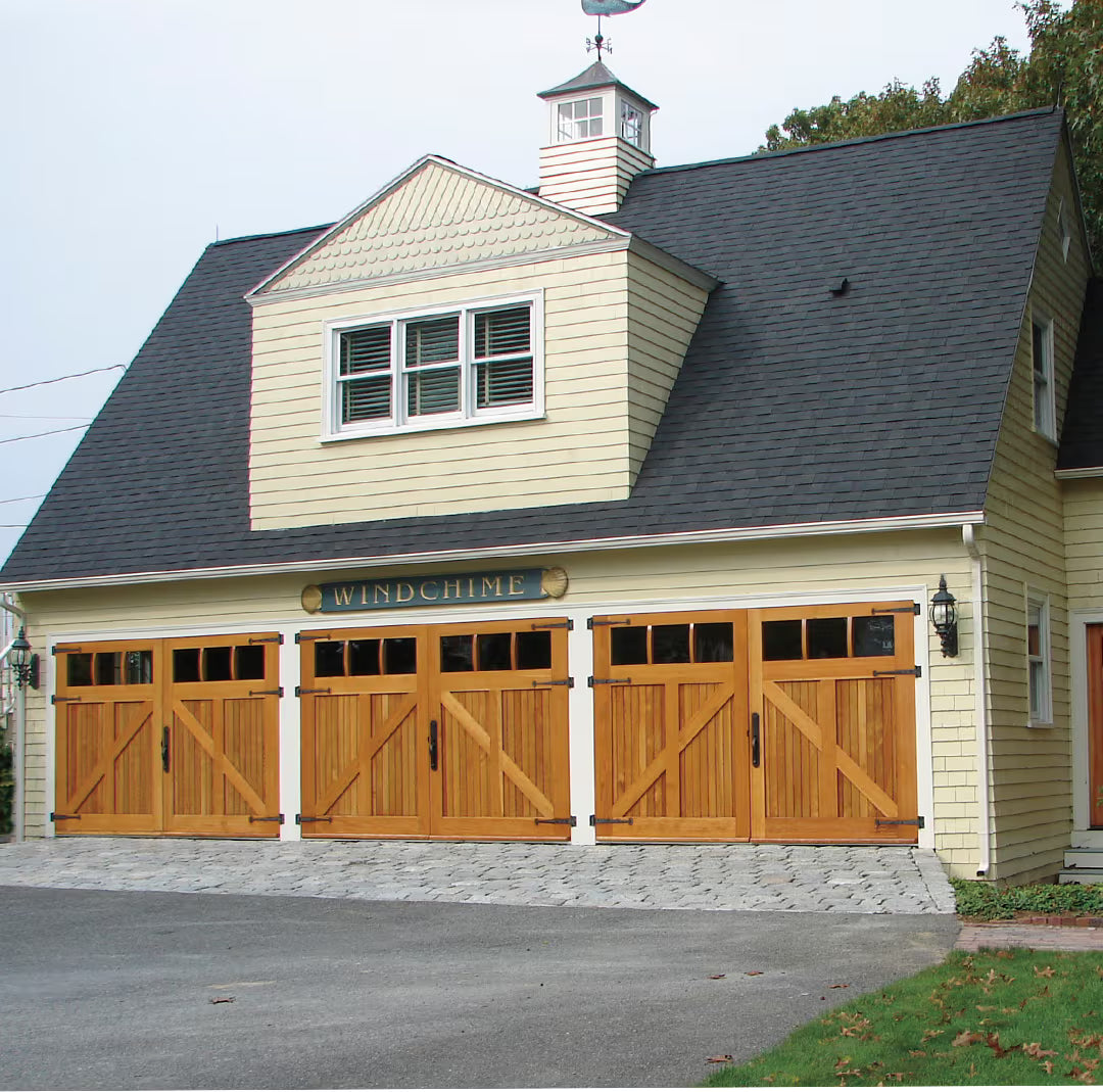 Three carriage garage doors with Z-brace detailing, clear glass panels, and strap hinges, installed side by side on a residential exterior in daylight.