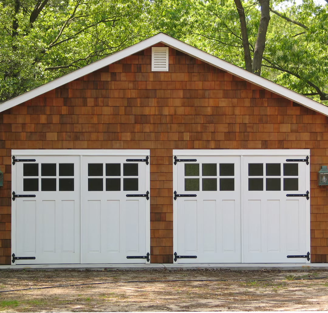 Double Craftsman-style carriage garage doors with clear glass panels and strap hinges, shown on a residential exterior in natural daylight.
