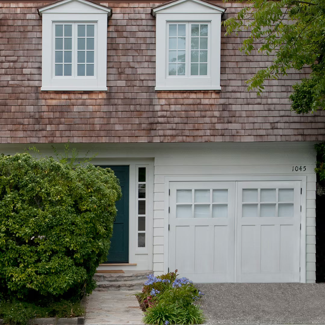 White Craftsman-style carriage garage door with a flat panel design and no visible hardware, shown on a residential exterior in daylight.