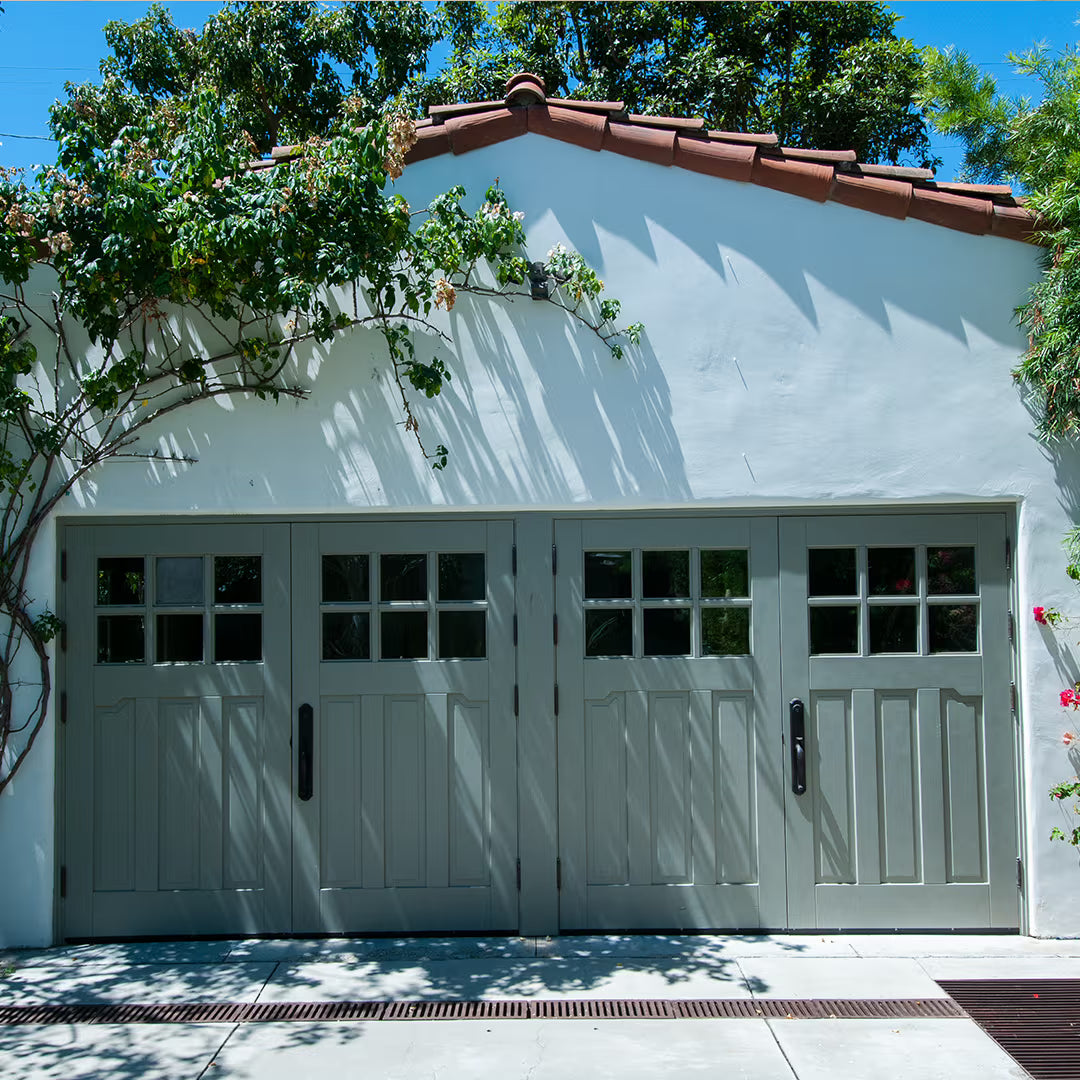 Green Craftsman-style carriage garage door with clear glass panels, installed on a residential exterior in natural daylight.