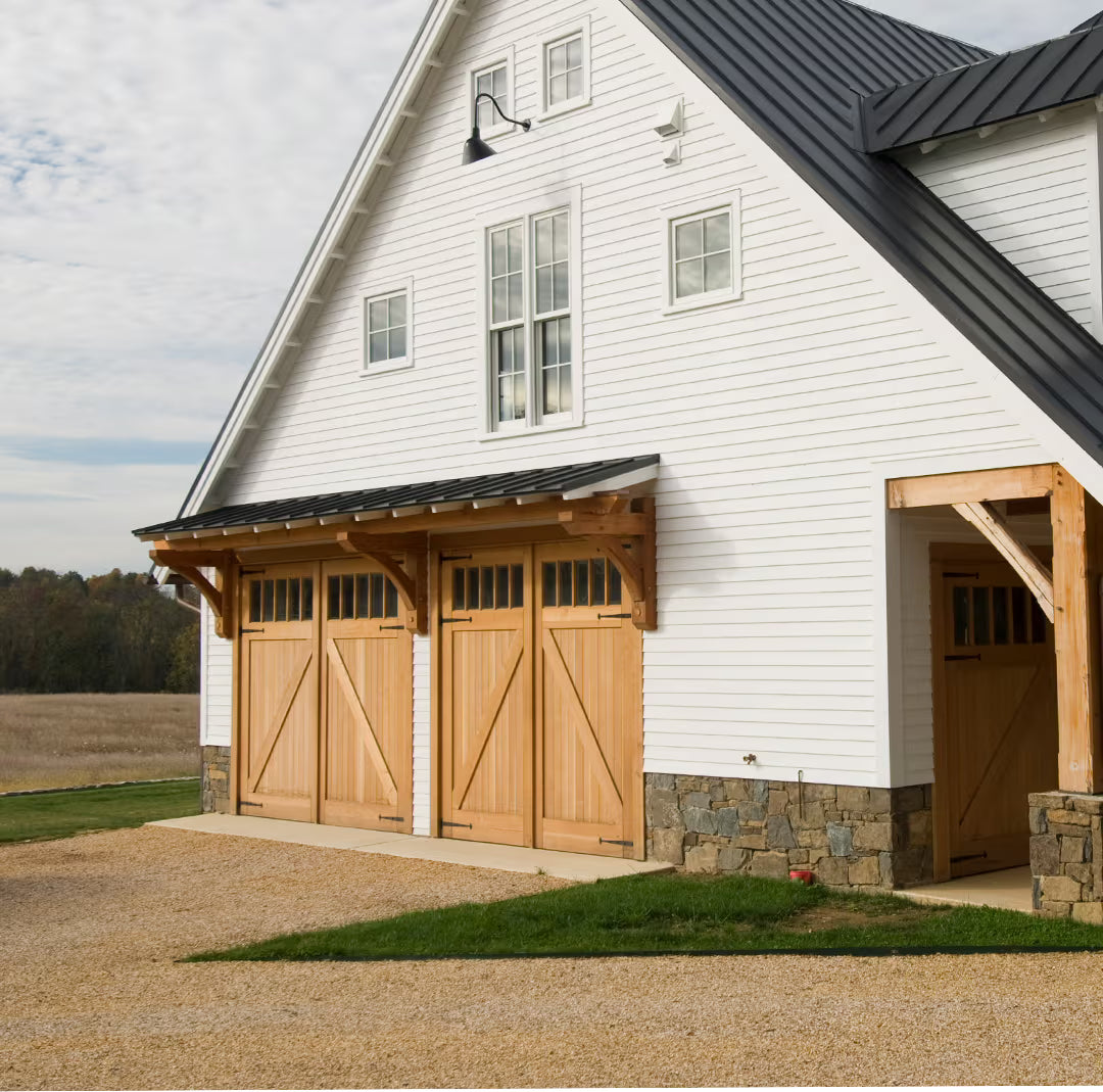 Set of unfinished Z-brace carriage garage doors with long strap hinges, installed on a residential exterior in natural daylight.