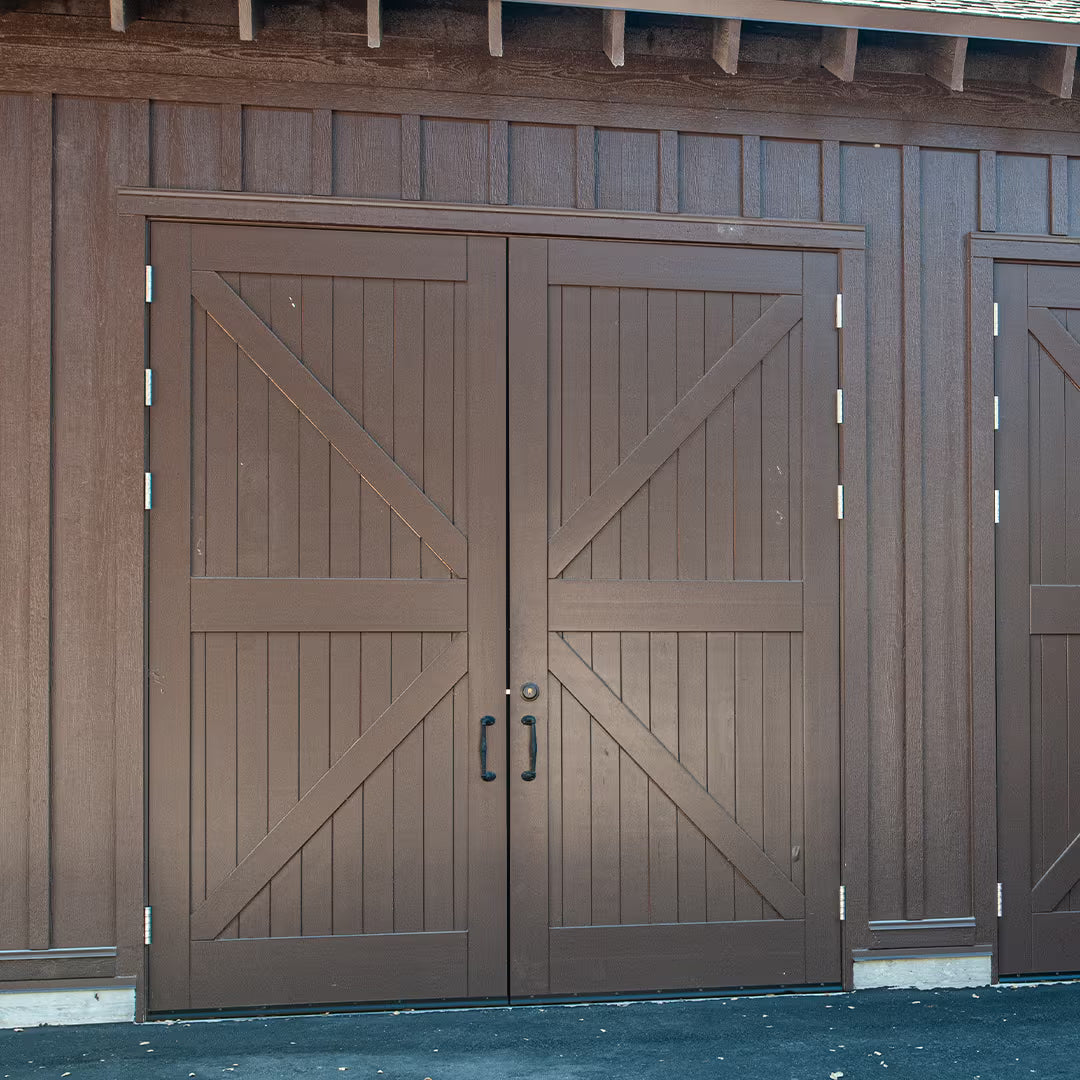 Brown painted carriage-style garage door with a British X plank design, installed on a commercial building exterior in daylight.