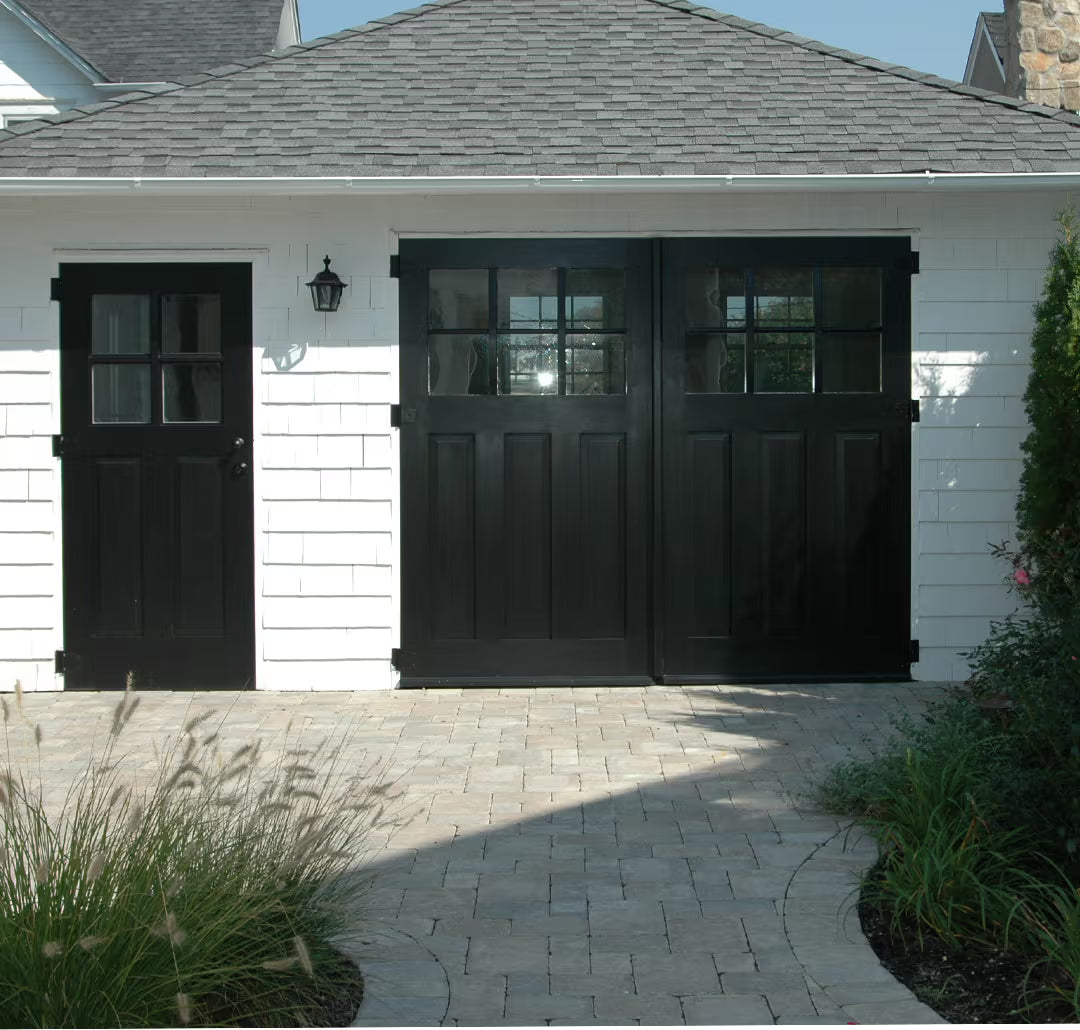 All-black carriage garage door with matching black entry door, shown on a modern residential exterior in daylight.