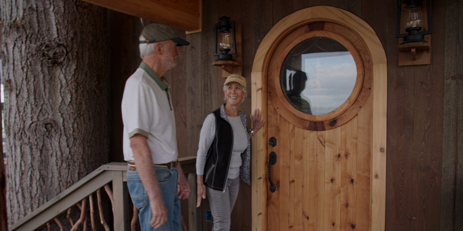 2 people smiling at each other in front of a Round Top Door with a Window and custom art installed into the entry way of a tree house
