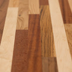 A long, horizontal wood wall art piece made of various solid colors and patterns in reds, browns, yellows, and other earth tones. The background is white with no shadows or textures on it. This artwork would be used as an accent for the dining room table, sitting under that wall art, and to match its color scheme.