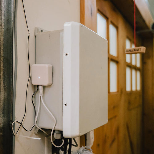 White Franklin Smart Home Connector mounted on a wall with cables connected, blurred wooden carriage door in the background.
