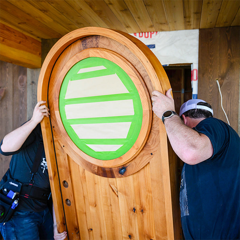 two craftsmen tilt a round top entry door into an opening. 