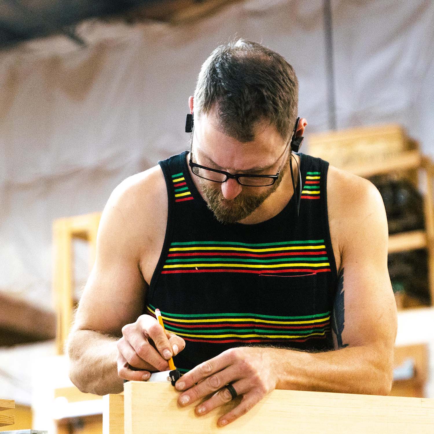 Craftsman with a tank top making marks with a pencil on a wood slab at RealCraft's wood shop.